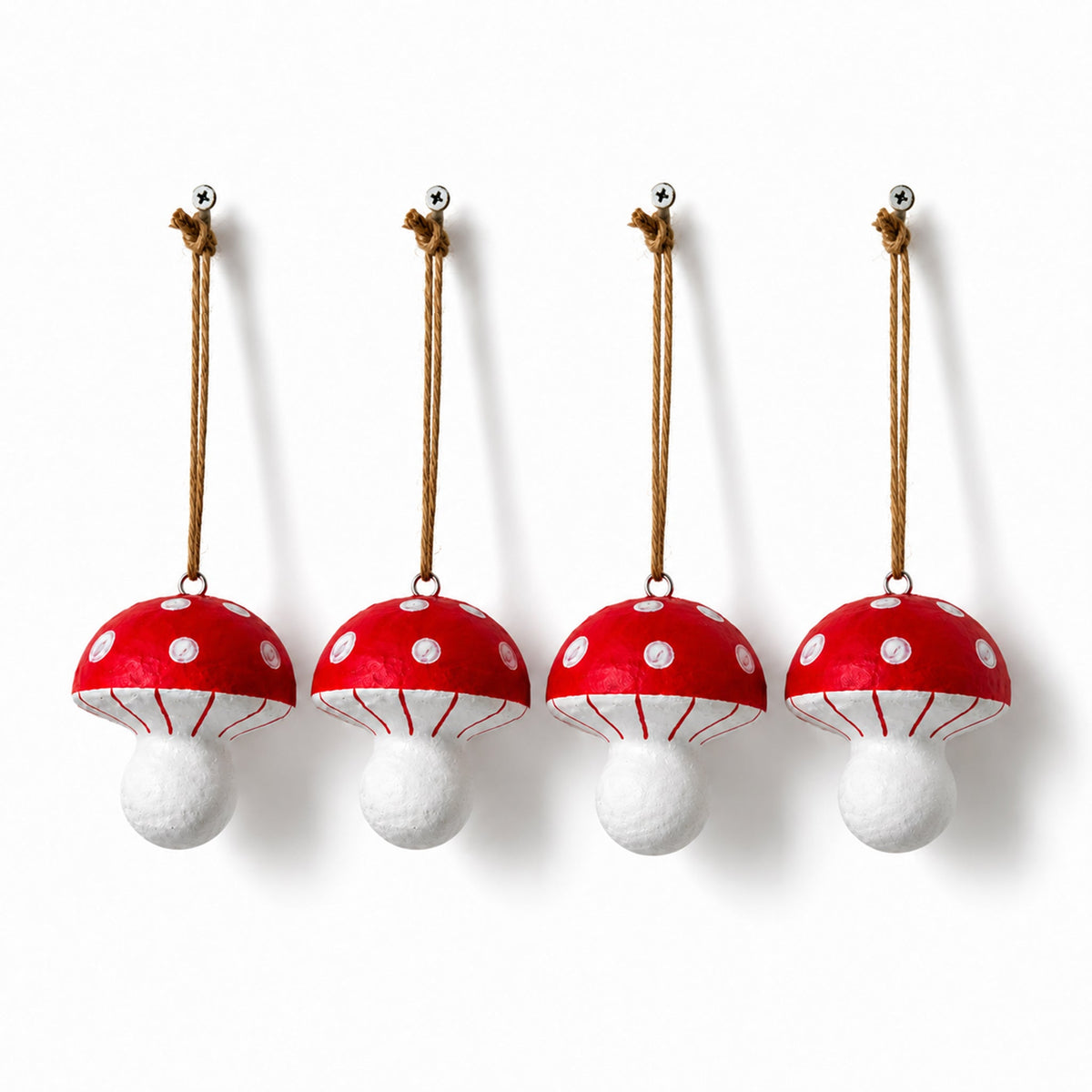 Four red and white toadstool Christmas decorations hanging from jute loops against a plain white background