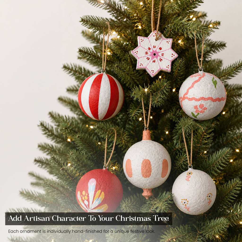 Handmade red and white folk art paper mache Christmas baubles hanging on lit Christmas tree — artisan festive ornaments UK