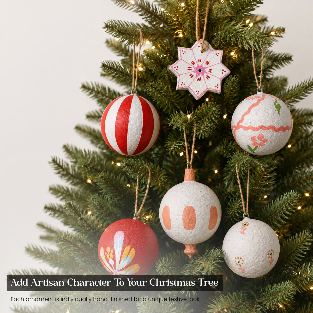 Handmade red and white folk art paper mache Christmas baubles hanging on lit Christmas tree — artisan festive ornaments UK