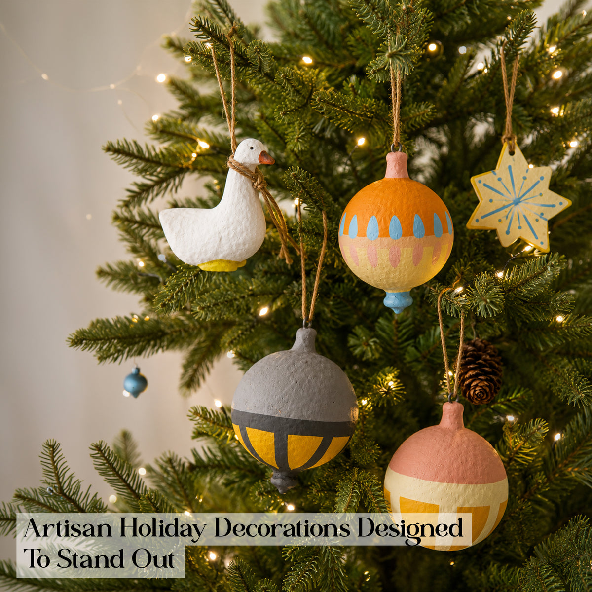 Whimsical handmade Christmas baubles hanging on lit Christmas tree – goose ornament, orange folk bauble and star charm, artisan holiday decorations