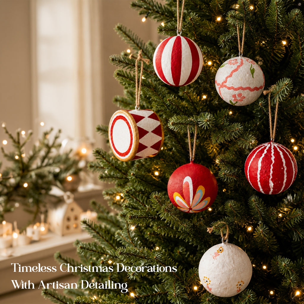 Handmade papier mâché Christmas baubles hanging on lit Christmas tree – red white folk art ornaments with jute hangers, artisan detailing