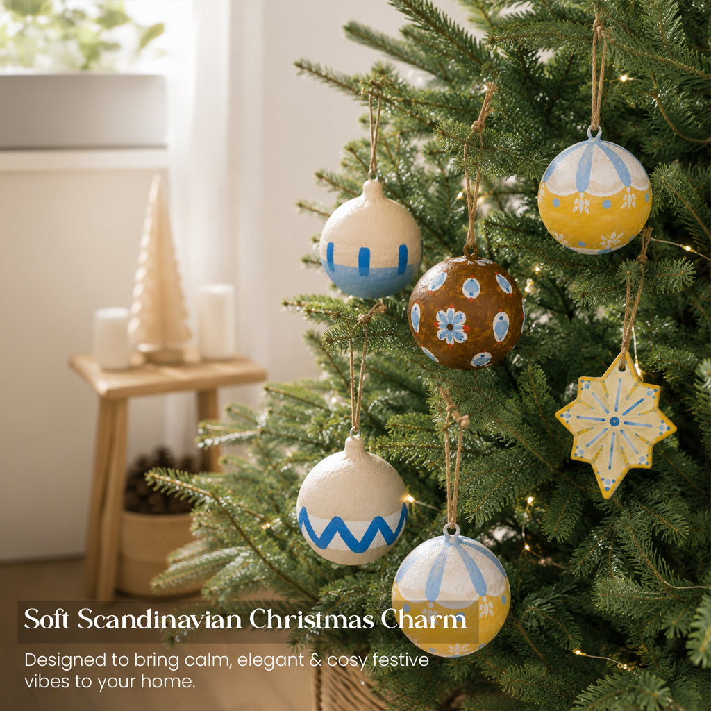 Soft Scandinavian hand-painted paper mache Christmas baubles on tree with fairy lights in cosy modern living room