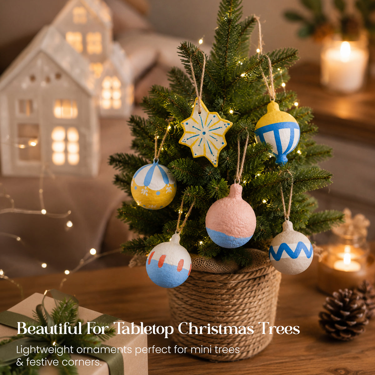 Lightweight paper mache Christmas baubles set on small tabletop mini Christmas tree with jute basket and fairy lights