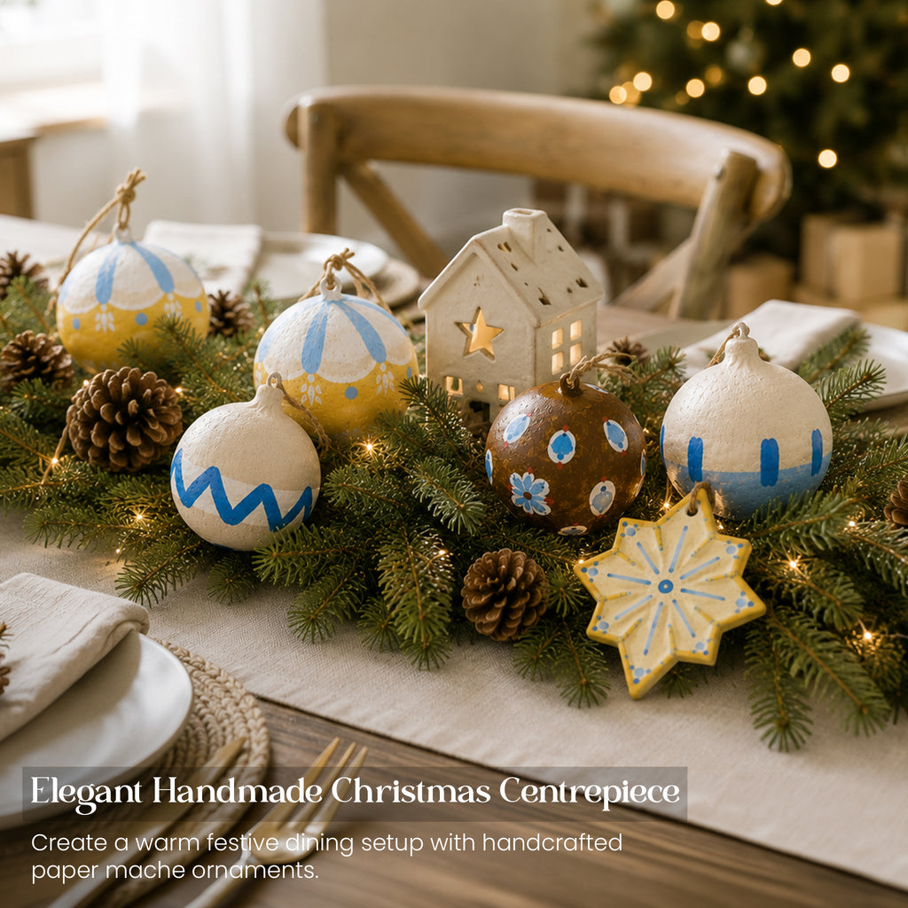 Artisan paper mache Christmas baubles as elegant dining table centrepiece with pine garland and fairy lights
