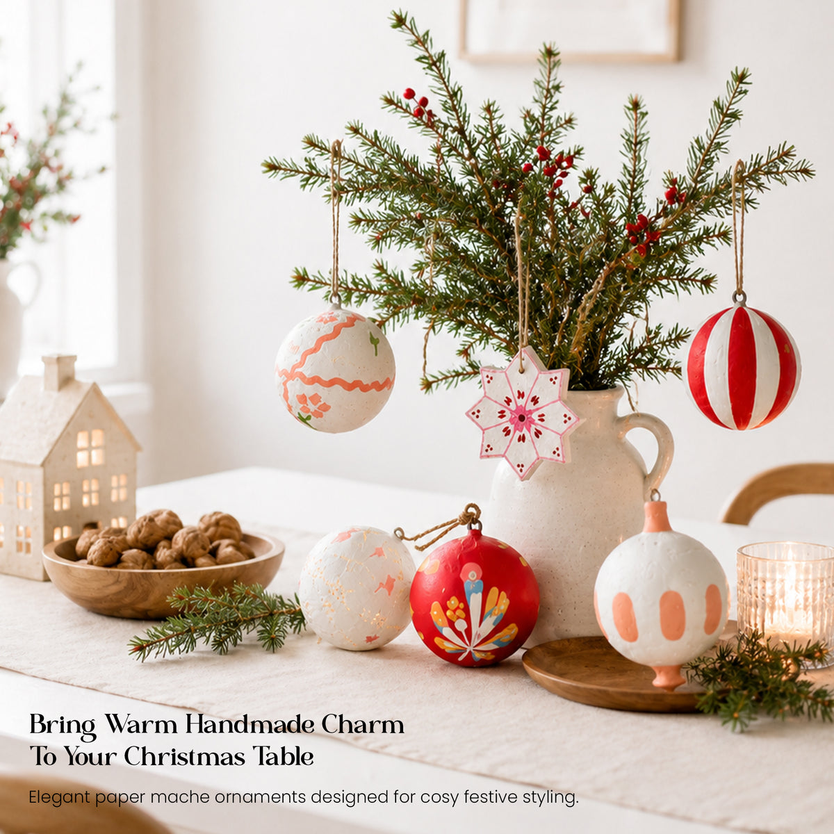Artisan hand-painted Christmas baubles in red and white styled on dining table with pine branches and vase centrepiece