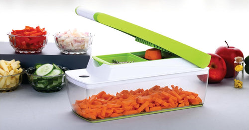 Chopper with the lid raised and a piece of carrot on the grid, with the clear container full of diced carrot